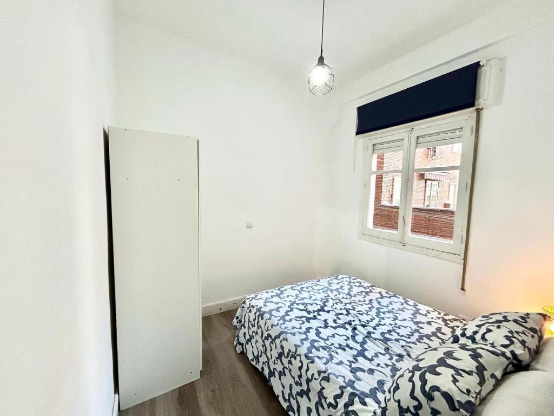 A bedroom with a bed, a window, a door, and a hanging light fixture.