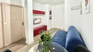 Una sala de estar con un sofá, un televisor, un mueble rojo y una puerta.