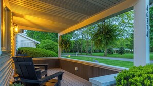 A covered porch with wooden flooring, a black chair, and a small table.
