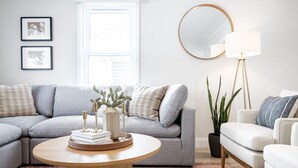 A modern living room with a grey sectional sofa, a round coffee table, a floor lamp, and a potted plant.