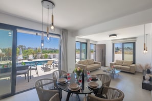 A modern living room with a dining area, large windows, and a view of a pool.