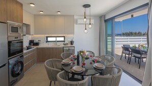 A modern kitchen with built-in appliances, a dining area with wicker chairs, and a balcony with a view. - Protaras Holiday Villa Ti39 (Paralimni)