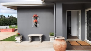 A modern building with a grey exterior, a metal window with red flowers, a stone bench, and a large terracotta pot on the porch. - Room-cozy Room With Separate Entrance an (Atherton)
