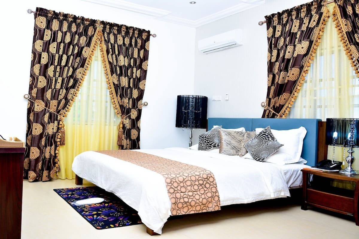 Une chambre d’hôtel avec un lit, des tables de chevet, un bureau et des rideaux.