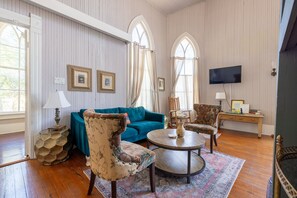 A room with a teal sofa, patterned armchairs, a round coffee table, and a TV mounted on the wall.