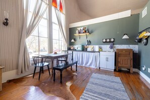 Una cocina con pisos de madera, una mesa de comedor con sillas, un banco y una encimera con electrodomésticos.