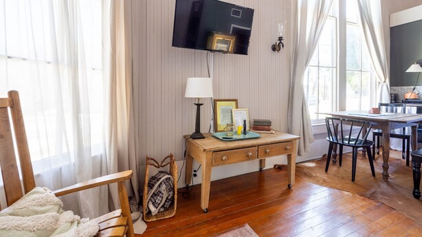 Una habitació amb escriptori de fusta, televisió penjada a la paret, cadira i taula de menjador amb cadires.
