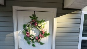 A white door with a wreath, a black doormat, and a vase with flowers on the porch. - Peaceful Comfort Home ideal for work trips and vacation. (Sanford)