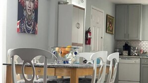 A dining area with a wooden table and white chairs, a painting on the wall, and a kitchen in the background. - Peaceful Comfort Home ideal for work trips and vacation. (Sanford)