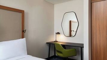 Een hotelkamer met een bed, een bureau, een groene stoel, een lamp en een spiegel aan de muur.