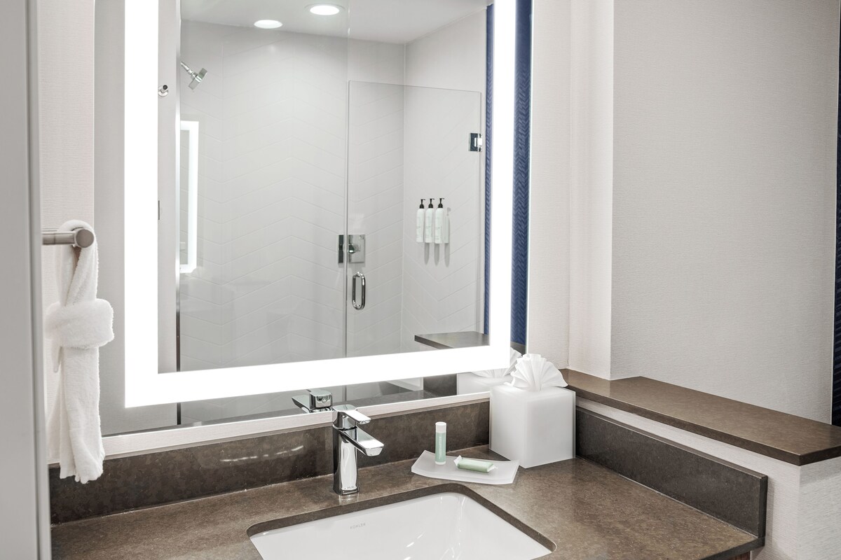 A modern bathroom with a large mirror, a sink, a towel rack, and a shower area.
