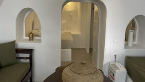 A room with a bed, a chair, a small table, and a wall-mounted heater. There are arched doorways leading to other rooms. - Fira 2-bed Villa, Sleeps 5 With Outdoor Hot Tub (Santorini)