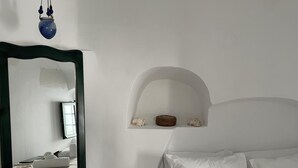 A bedroom with a bed, white pillows, a mirror with a black frame, and a shelf with decorative items. - Fira 2-bed Villa, Sleeps 5 With Outdoor Hot Tub (Santorini)