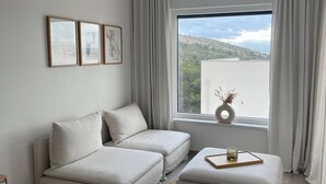 A modern bedroom with a sofa, a small table with a tray, and a view of a mountainous landscape through a large window. - Cozy Loft Studio With Rooftop, Seaview & Pool (Okrug)