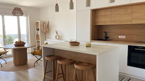 A modern kitchen with a central island, wooden stools, a built-in oven, and a window with a view. - Cozy Loft Studio With Rooftop, Seaview & Pool (Okrug)