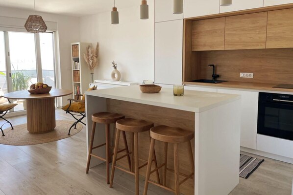 Una cucina moderna con isola centrale, sgabelli in legno, forno integrato e una finestra con vista.