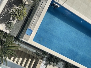 Una vista aerea di una piscina rettangolare con bordo piastrellato, circondata da un solarium con ghiaia e qualche pianta.