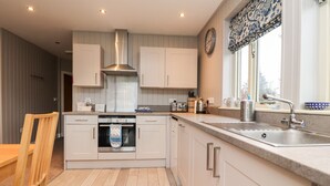 Une cuisine moderne avec des armoires blanches, une hotte de cuisinière en acier inoxydable, un four encastré, un évier doté d’un robinet contemporain et une fenêtre agrémentée de rideaux à motifs.