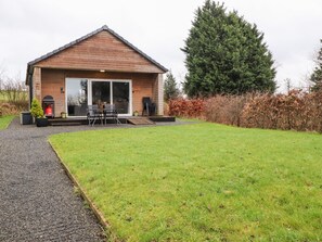 A modern house with a large glass door, a patio with outdoor furniture, and a well-maintained lawn. - Beech Lodge (Preston)