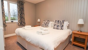 Une chambre d’hôtel avec un grand lit, deux tables de chevet, une fenêtre avec des rideaux et une lampe sur l’une des tables.