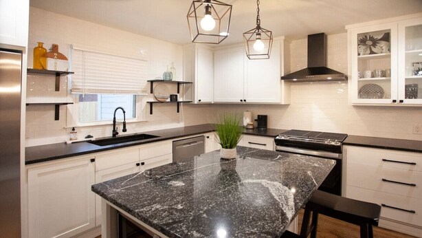 Une cuisine moderne avec des armoires blanches, des comptoirs en granit, une cuisinière noire et des luminaires suspendus.