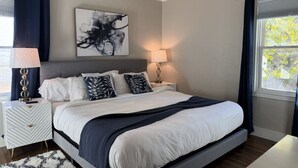 Une chambre à coucher avec un grand lit, deux tables de chevet, un ventilateur de plafond et une fenêtre avec des rideaux.