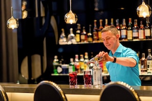 Um bartender prepara bebidas em um bar, com garrafas ao fundo.