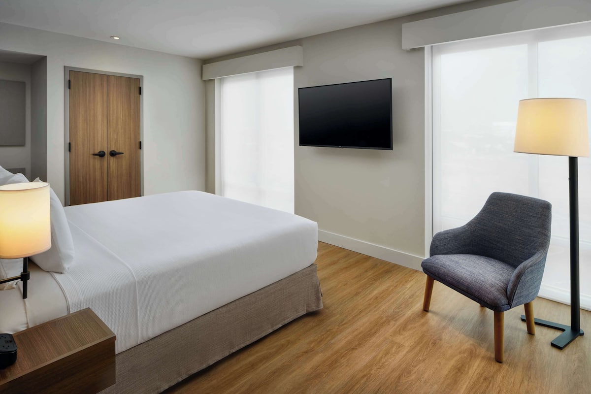Een hotelkamer met een bed, een stoel, een televisie en een lamp.