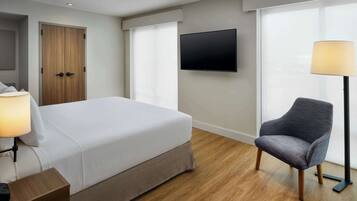 A hotel room with a bed, a chair, a TV, and a lamp.