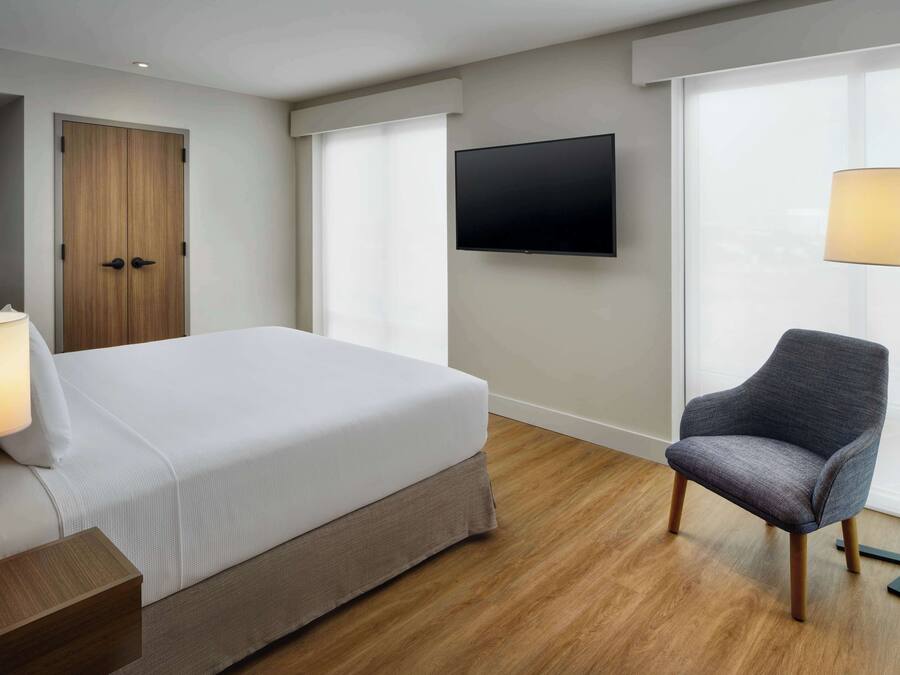 A hotel room with a bed, a chair, a TV, and a lamp.
