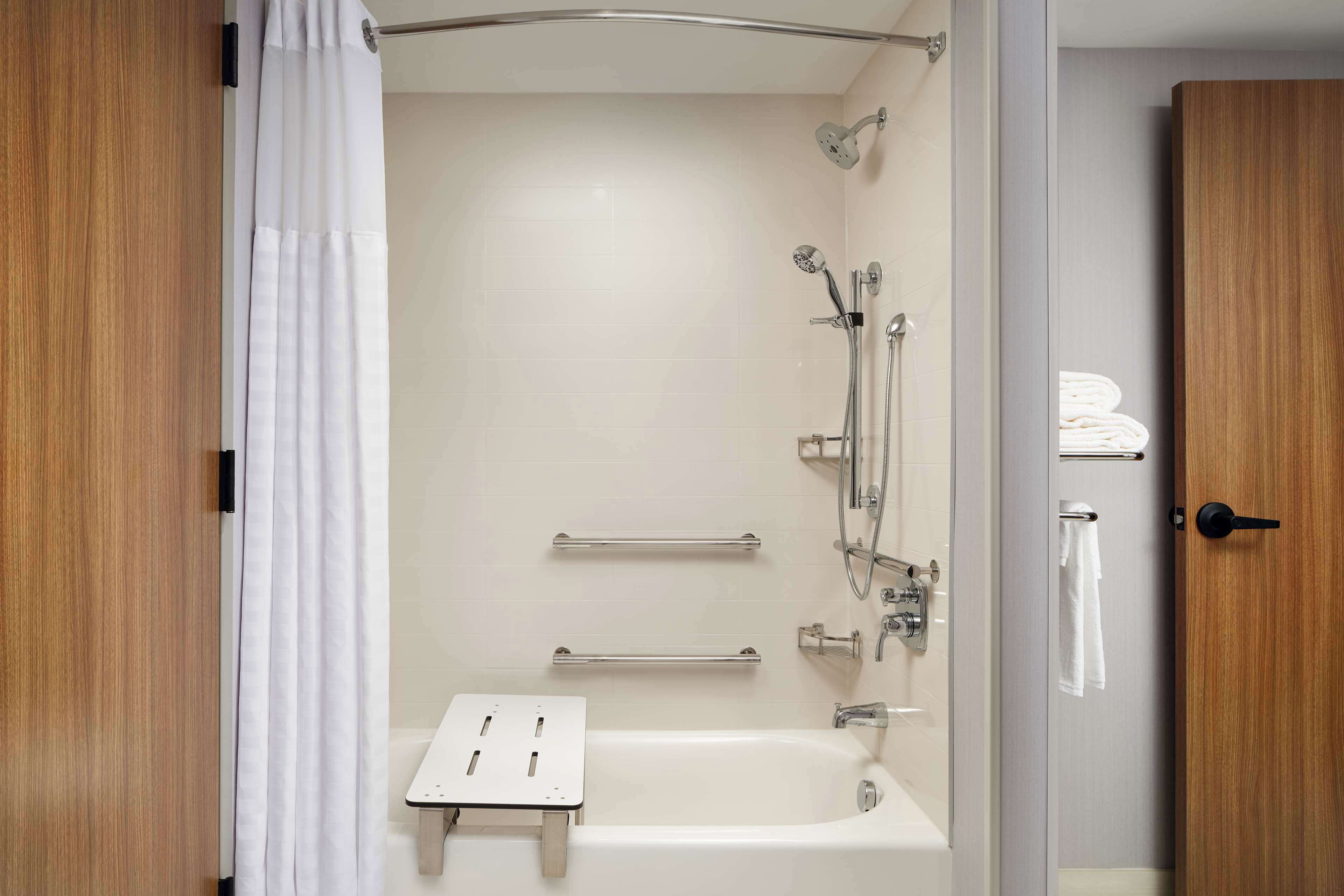 A modern bathroom with a bathtub, shower, and handrails.
