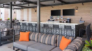 Een moderne buitenruimte met een bar, zachte zitplaatsen en een toonbank met barstoelen.