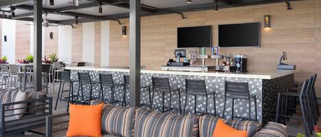 A modern outdoor seating area with a bar, cushioned seating, and a counter with bar stools.