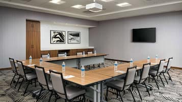Ein Konferenzraum mit einem langen Tisch, Stühlen, einem Projektor und einem Fernseher an der Wand.