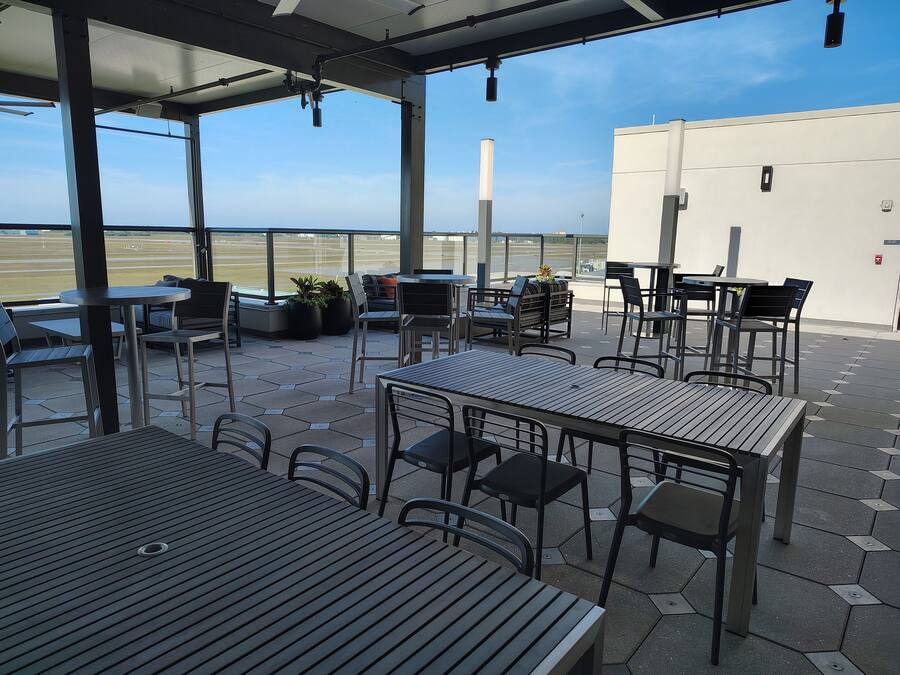 An outdoor patio area with tables and chairs, a view of the airport, and a building in the background.