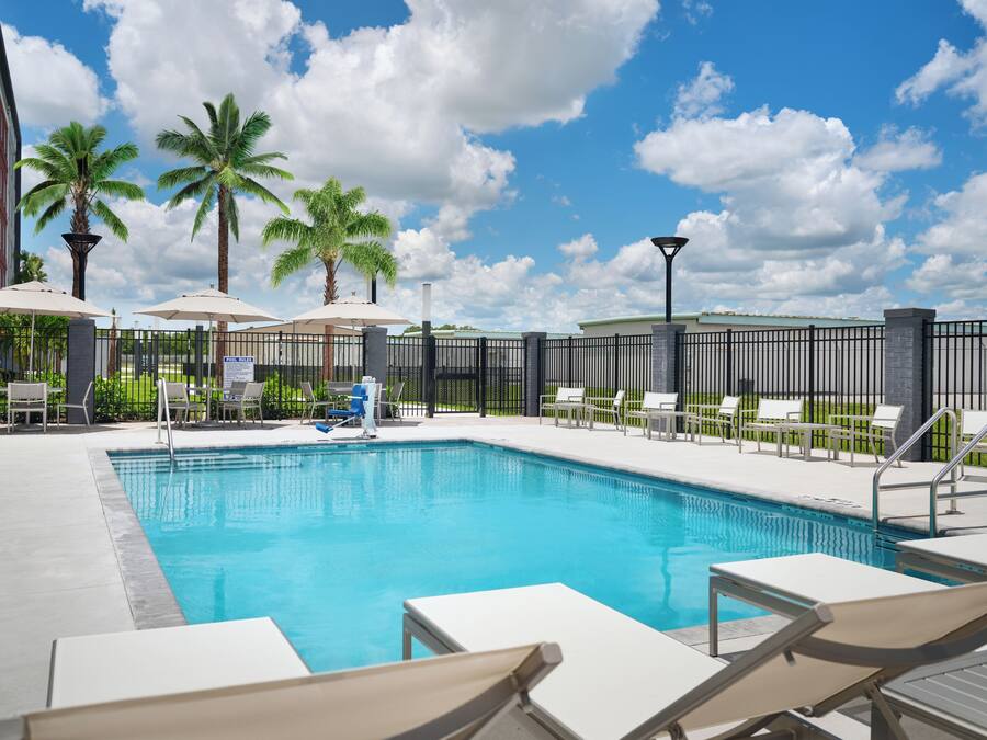 A pool area with lounge chairs and umbrellas, surrounded by a fence and palm trees.