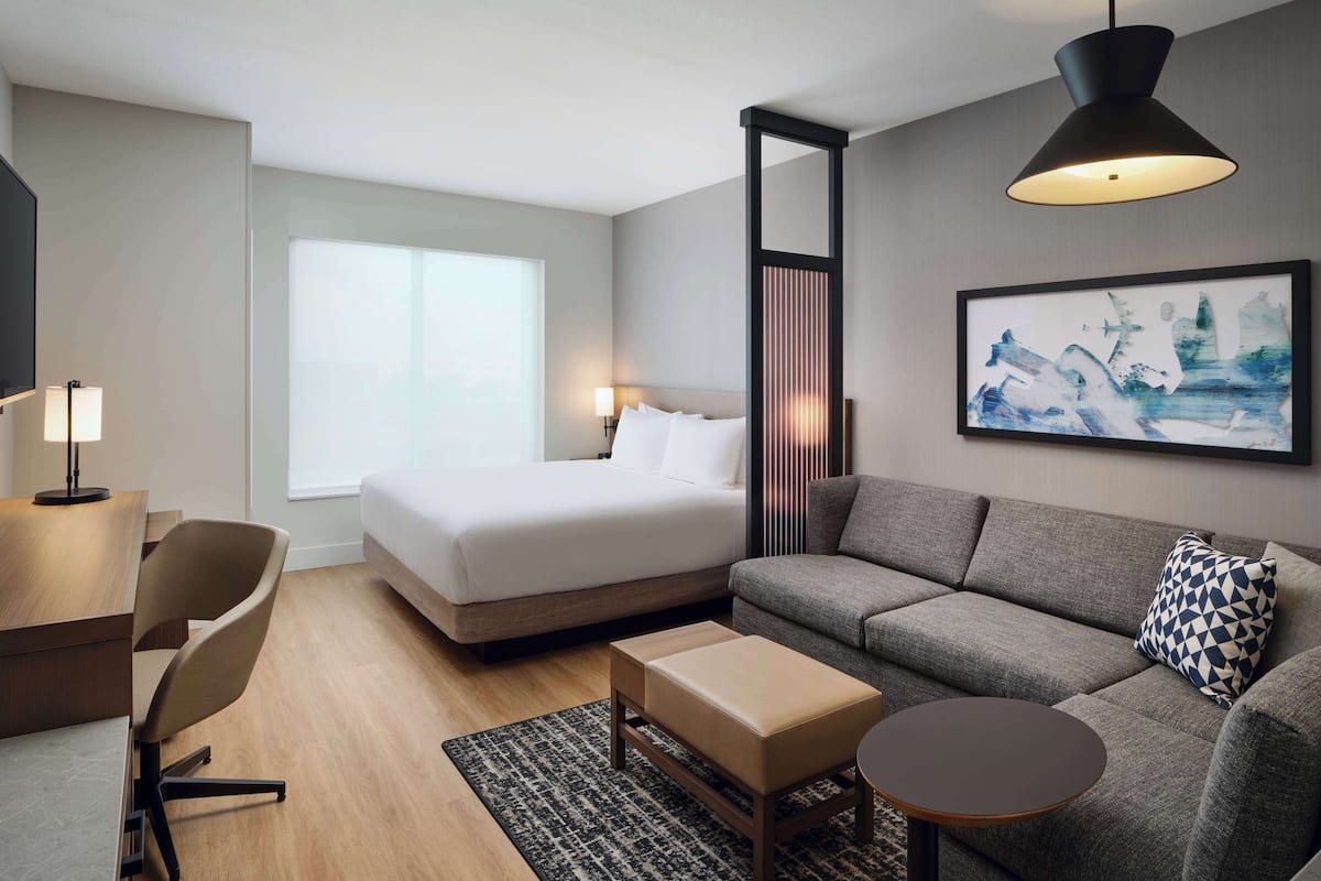 Een moderne hotelkamer met een bed, een bank, een bureau en een groot raam.
