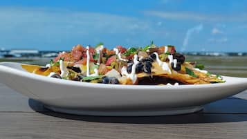 Nachos sobre un plato blanco con diversos ingredientes, colocados sobre una mesa de madera con un cielo despejado y un aeropuerto distante al fondo.