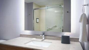 A modern bathroom with a large mirror, a sink, and a glass shower enclosure.