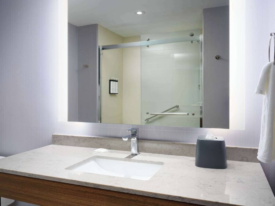 A modern bathroom with a large mirror, a sink, and a glass shower enclosure.