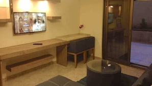 A living room with a TV, a bench, a glass coffee table, and a sliding glass door. - The Royal Luxury Queen Terrace 1 (Amman)