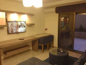 A living room with a TV, a bench, a glass coffee table, and a sliding glass door.