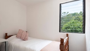A single bed with a wooden headboard, a white mattress, and a pink blanket. A window with a view of trees is visible. - Room in Guest Room - Cuarto En Las Lomas! (Naucalpan)