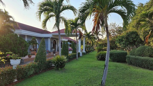 Un jardín bien cuidado con palmeras y una casa con techo de tejas rojas.
