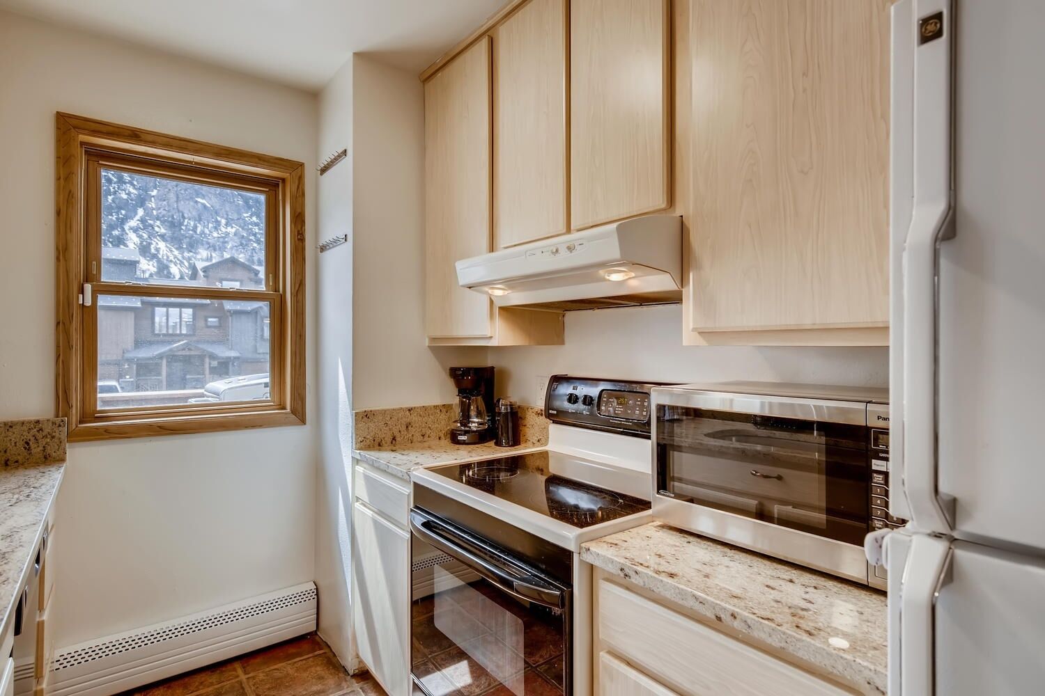 A compact kitchen with wooden cabinets, a built-in oven, a microwave, and a coffee maker.