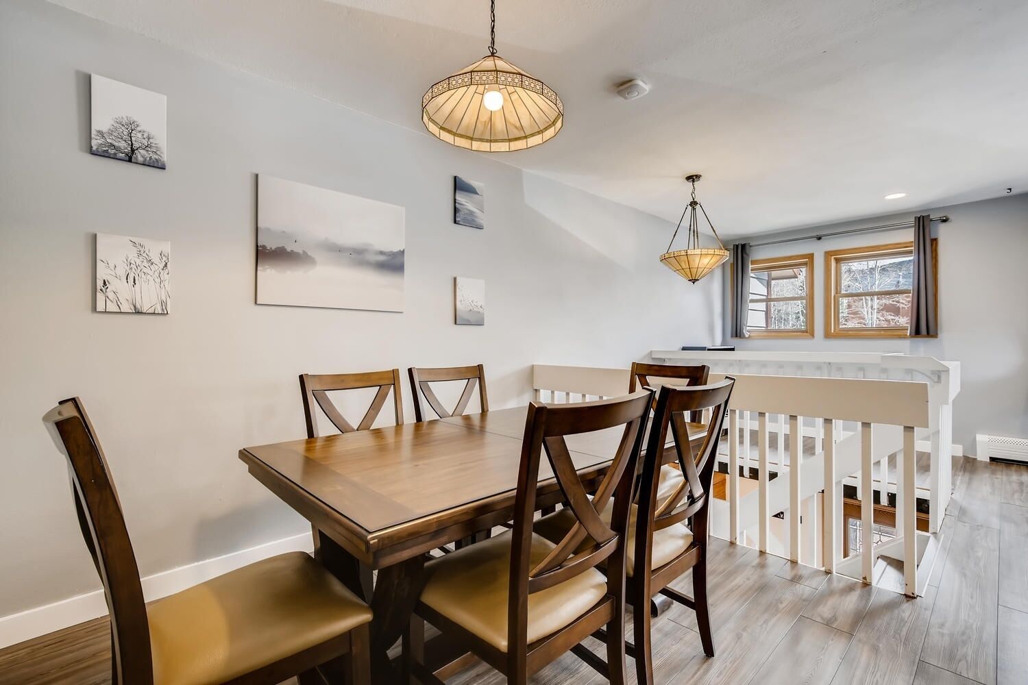 A dining area with a wooden table and chairs, a hanging light fixture, and artwork on the walls.