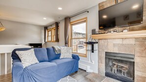 A modern living room with a blue sofa, a fireplace, a mounted TV, and a view of the outside. - Mount Royal Condos #501 2 Bedroom Condo by RedAwning (Frisco)