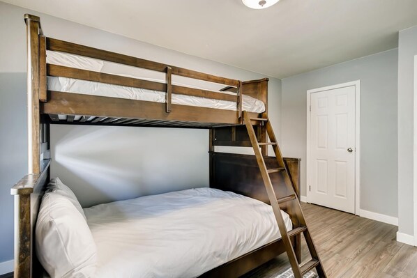 Una cama litera con una escalera de madera en una habitación con paredes de colores claros y una puerta blanca.