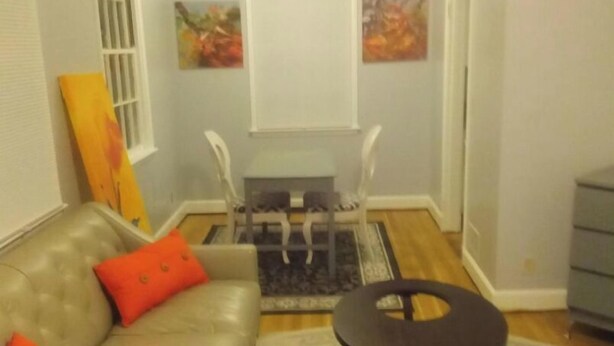 Una sala de estar con un sofá gris, cojines naranjas, una mesa de centro oscura y una alfombra estampada.