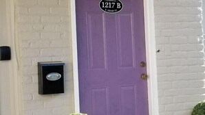 A white brick building with a purple door labeled "1217 B E Henry St." - All Inclusive Extended Stays Only! #1 (Savannah)